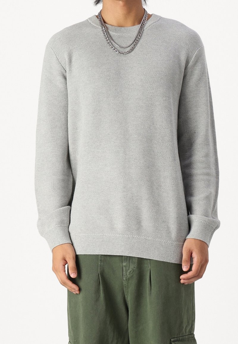 Maglione grigio chiaro con un motivo a maglia testurizzato, scollo rotondo, e polsini e orlo a costine. Abbinato a pantaloni cargo verdi.