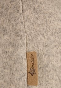 Beige wool fabric with visible seam and a brown rectangular label featuring a star and the word "Stortaler" in cursive.