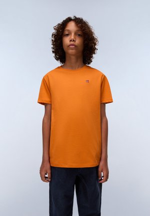 Orange cotton t-shirt with a round neckline and short sleeves, featuring a small Norwegian flag patch. Paired with dark jeans.