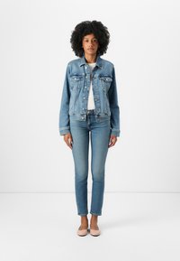 Jachetă din denim de culoare albastru deschis, cu două buzunare frontale, asociată cu blugi albaștri deschiși, ajustați. Modelul poartă balerini nude și un tricou alb.