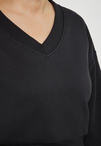 Maglione nero a V con maniche lunghe, realizzato in tessuto liscio, con una vestibilità comoda e scollo a costine, texture liscia.