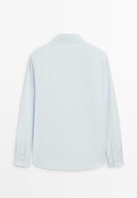 Camicia a maniche lunghe azzurro chiaro, realizzata in tessuto strutturato. Presenta un colletto, polsini con bottoni e un orlo curvo. Nessun dettaglio di design frontale visibile.