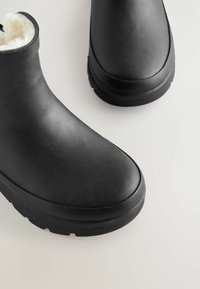 Bottes noires imperméables avec tige synthétique texturée, bout rond et doublure en peluche. Semelle en caoutchouc durable avec un motif de traction léger.