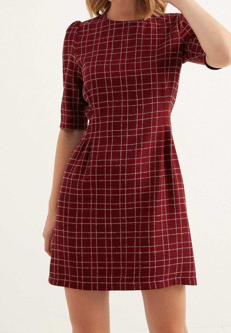 Rød ternet kjole med korte ærmer, med en struktureret silhuet og en subtil tekstur, fremhævet af hvide gitterlinjer.