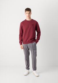 Sudadera burdeos con cuello redondo, combinada con pantalones a rayas verticales grises y zapatillas blancas. La tela parece suave y deportiva.