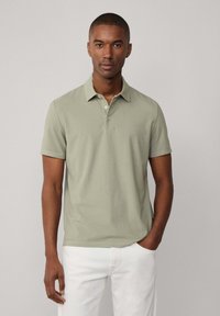 Polo in tessuto verde chiaro con vestibilità rilassata. Maniche corte e polo con patta a tre bottoni. Abbinato a pantaloni bianchi.