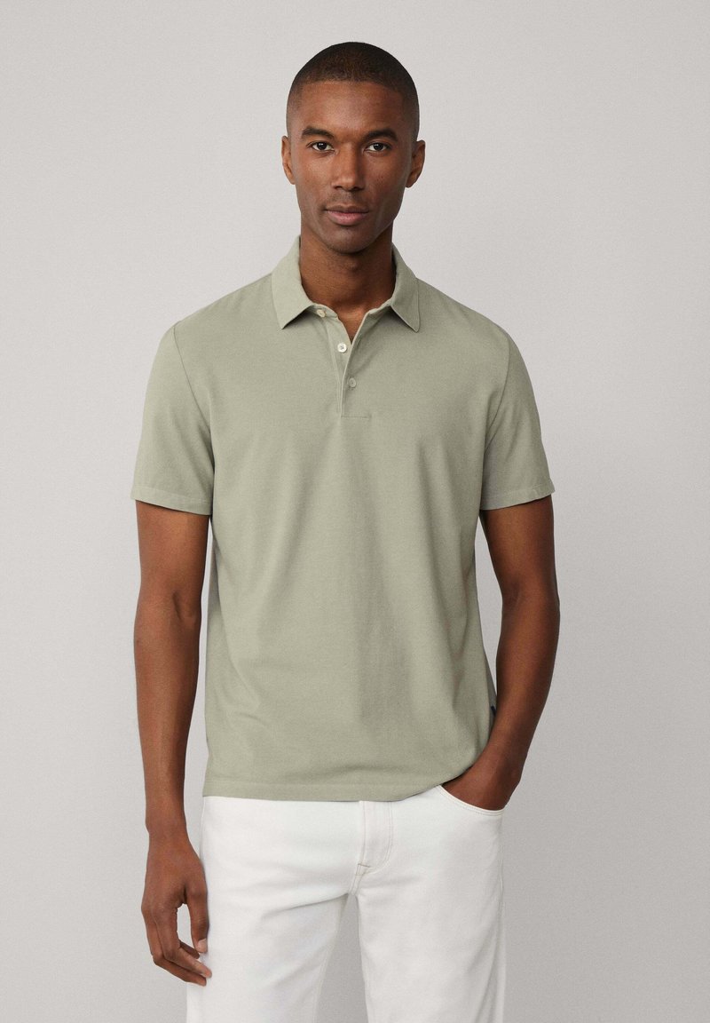 Polo in tessuto verde chiaro con vestibilità rilassata. Maniche corte e polo con patta a tre bottoni. Abbinato a pantaloni bianchi.
