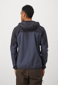 Mørkeblå jakke med hette, med fargeblokkdesign i mørkere og lysere nyanser. Laget av glatt, elastisk stoff med tettsittende ermer.