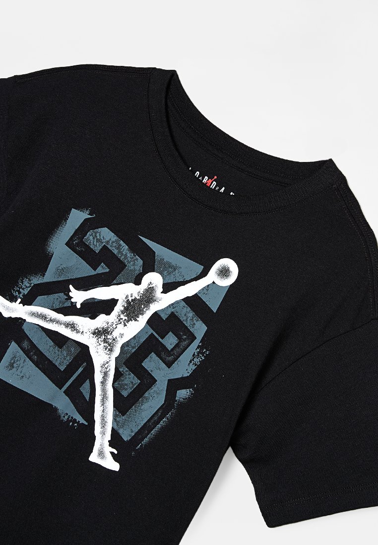 T-shirt in cotone nero con una grafica di una figura in salto con un pallone da basket. Lo sfondo presenta un motivo geometrico blu. Design a girocollo.