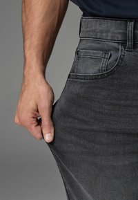 Schwarze Denim-Jeans mit einer sanft ausgeblichenen Optik, mit einer Gesäßtasche und von einer Hand am Bund gezogen.