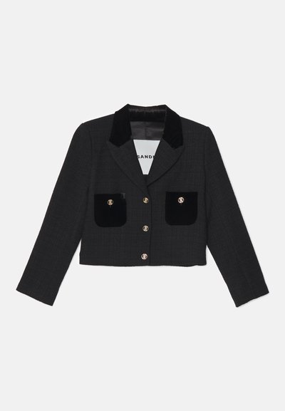 Κομμένο μαύρο σακάκι σε υφασμάτινη υφή. Διαθέτει βελούδινο γιακά, δύο μπροστινές τσέπες με βελούδινα στοιχεία και διακοσμητικά χρυσά κουμπιά.