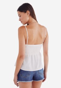 Weißes, ärmelloses Oberteil mit einem gerafften Oberteil und einem Peplum-Saum, kombiniert mit Denim-Shorts. Verfügt über dünne, verstellbare Träger und eine weiche Textur.