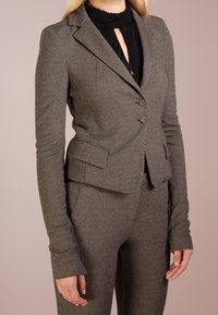 Grå texturerad blazer med en figursydd design, som har tre knappar, slagkrage och sidofickor. Accenterad av en klassisk svart underskjorta.