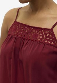 Bordeaux mouwloos topje met kantdetail bij de halslijn en soepel vallende stof, met dunne schouderbandjes en een ontspannen pasvorm.