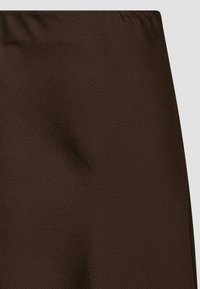 Bruine textuurstof met een subtiel patroon, voorzien van een gladde afwerking en een licht elastische tailleband. Over het geheel genomen een uniforme kleurpresentatie.
