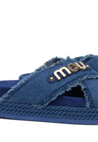 Sandalo scivolante in denim blu con bordi sfilacciati, branding in tonalità oro e suola in gomma blu testurizzata con dettagli in corda.