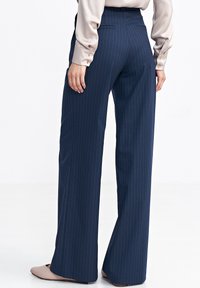 Granatowe spodnie o szerokich nogawkach z pionowymi prążkami, wykonane z gładkiej tkaniny. Posiadają tylne kieszenie oraz wysoki stan zapewniający dopasowany krój.