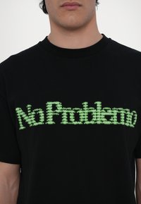 Tricou negru din bumbac, cu un design grafic verde care spune "No Problemo" într-un font stilizat, pe piept. Mâneci scurte.