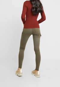 Ribbad vinröd långärmad topp kombinerad med olivgröna skinnybyxor med bakfickor och sidofickor. Beiga sneakers med vita detaljer.