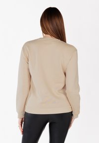 Felpa beige con collo a giro e polsini a costine. Realizzata in tessuto morbido, presenta una superficie liscia e un design aderente.