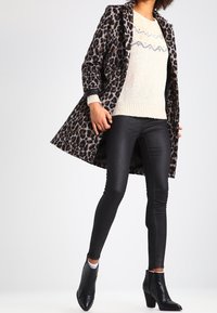 Leopardmönstrad kappa med strukturerade slag, krämfärgad stickad tröja med fair isle-mönster, figurnära svarta leggings och svarta klackiga ankelstövlar.