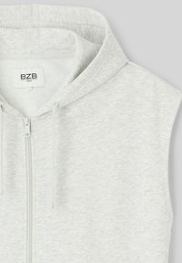 Haut sans manches gris clair avec fermeture éclair frontale complète, capuche et cordons de serrage ; fabriqué à partir d'un tissu doux et texturé. L'étiquette indique "BZS Loose."