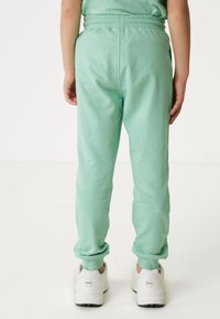 Mintgrüne Jogginghosen aus weichem Material mit einem bequemen Bund. Die Säume sind schmal zulaufend, und die Person trägt weiße Sneaker.