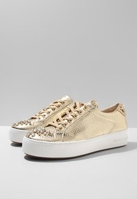 Zapatillas de serpiente doradas con textura, con cordones beige, suelas de plataforma blancas y adornos de cristal en la puntera y el tacón.