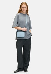 Jasnoniebieska torebka typu crossbody o gładkiej teksturze, prostokątnym kształcie i srebrnym okuciu. Połączona z szarym, oversize'owym t-shirtem i czarnymi spodniami.