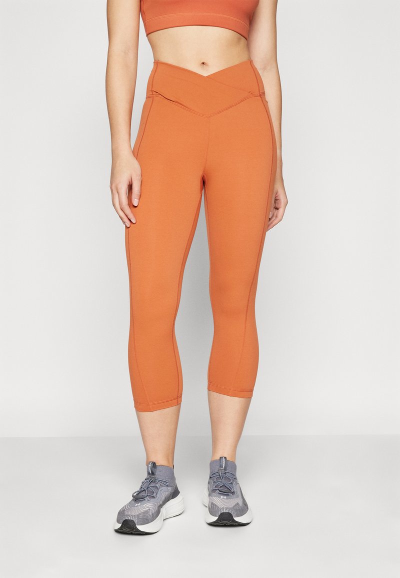 Oranžové vysoké capri legíny so zapínaním na páse a bočnými švami. Vyrobené z elastického materiálu, ideálne na cvičenie.