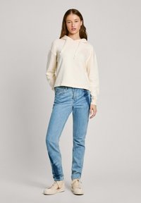 Sweatshirt creme com cordões, corte descontraído. Jeans azul claro com corte clássico. Ténis brancos com detalhes em bege. Textura suave ao todo.