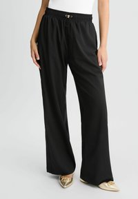 Zwarte wijde broek met een elastische tailleband en trekkoord. De stof is soepel en lichtgewicht, aangevuld met goudkleurige hardware.