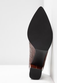 Botte en cuir marron à bout pointu avec texture crocodile, présentant une semelle noire et un talon carré, taille 4½ marquée sur la semelle.
