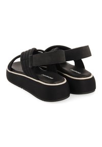 Svarta plattformsandaler med tjocka, texturerade remmar och en bred gummisula. Har vita accentstygn längs kanten.