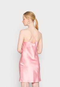 Vestido rosa de cetim com finas alças cruzadas nas costas, até ao joelho, textura suave e um silhueta simples, mostrando o design das costas.