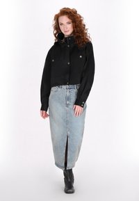 Jachetă neagră scurtă cu nasturi îmbinați, asortată cu o fustă din denim albastru deschis, cu o deschidere în față și bocanci negri până la gleznă.
