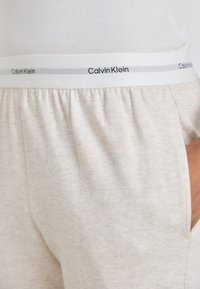 Pelēkās Calvin Klein sporta bikses ir izgatavotas no mīksta, melnbalti raibā auduma, ar elastīgu jostu un zīmola detaļām baltā un pelēkā krāsā.