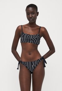 Black bikini set featuring a cropped top with bold white text and adjustable straps, paired with tie-side bottoms. Smooth fabric texture.