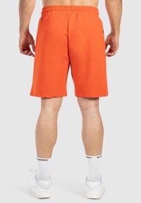 Oranssi urheilushortsit, joissa on joustava vyötärö ja sivutaskut, yhdistettynä valkoisiin lenkkikenkiin ja nilkkasukkiin.