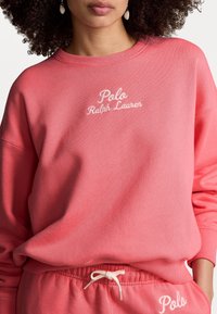 Korallfärgad sweatshirt med broderad "Polo Ralph Lauren"-logotyp, ribbad mudd och avslappnad passform, i kombination med matchande sweatpants med dragsko.