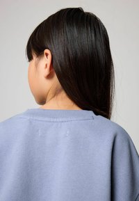 Sudadera de color púrpura claro con cuello redondo y puños de canalé. La tela parece suave, con una ligera textura y detalles de costura visibles.