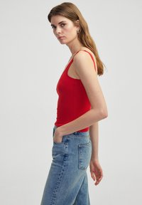 Top sin mangas ajustado rojo con tirantes finos, combinado con pantalones de mezclilla de tiro alto en un tono azul claro. Tela suave, diseño sencillo, que resalta una silueta limpia.