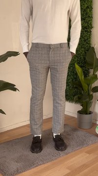 Pantalones a cuadros grises con un ajuste entallado, que presentan un frente plano y dos bolsillos laterales. Combinados con zapatos negros y calcetines blancos.
