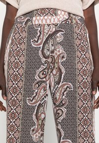 Calças largas com um padrão paisley em tons de vermelho, verde e preto. A cintura é elástica com um tecido estampado.