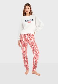 Sudadera blanca con "THE BEATLES" y acentos gráficos, combinada con pantalones rojos con estampado de texto repetido. Material de felpa casual.