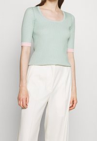 Haut court vert menthe côtelé à manches courtes avec un col dégagé et des poignets roses, associé à un pantalon blanc taille haute pour un look décontracté.
