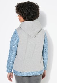 Sweat-shirt gris avec une manche et un ourlet à motifs floraux bleus. Il présente une texture douce, une coupe standard et une capuche avec cordon de serrage.