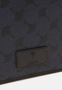 Texturiert blauer Stoff mit einem sich wiederholenden Muster, verziert mit einer schwarzen Namensschild-Prägung mit einem Logo. Akzentuiert mit klaren Linien.