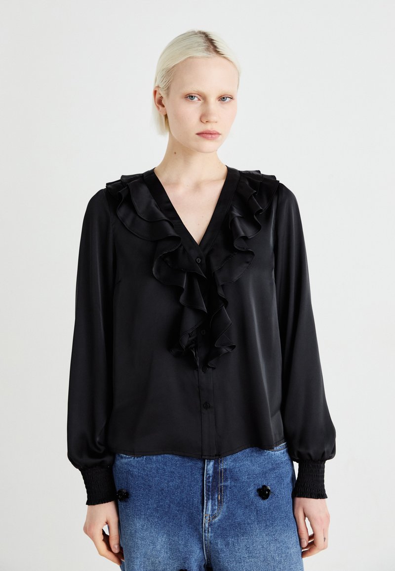 Blusa nera in satin con scollatura a V arricciata, maniche lunghe e chiusura con bottoni. Presenta polsini testurizzati e un tessuto liscio con una finitura lucida.