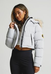 Balta pūta jakas ar noņemamu kažokādas kapuci, ar rāvējslēdzēja priekšpusi, sānu kabatām un zīmola rāvējslēdzēja vilcēju; īss piegriezums un quilted tekstūra.